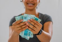 Mulher com 100 reais na mão.