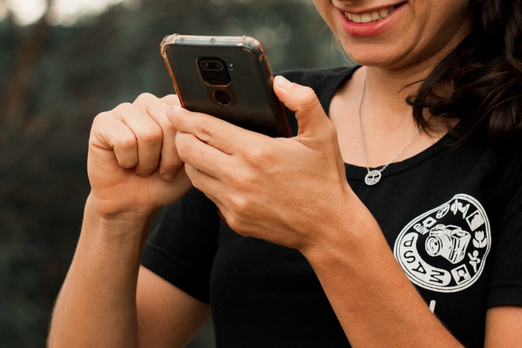 Mulher meia idade sorrindo com o celular na mão. 